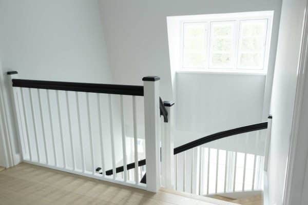 Trætrappe udformet som en halvsvingstrappe med hvide trappe vange, sort trappegelænder og trappetrin i eg fra Vejletrappen